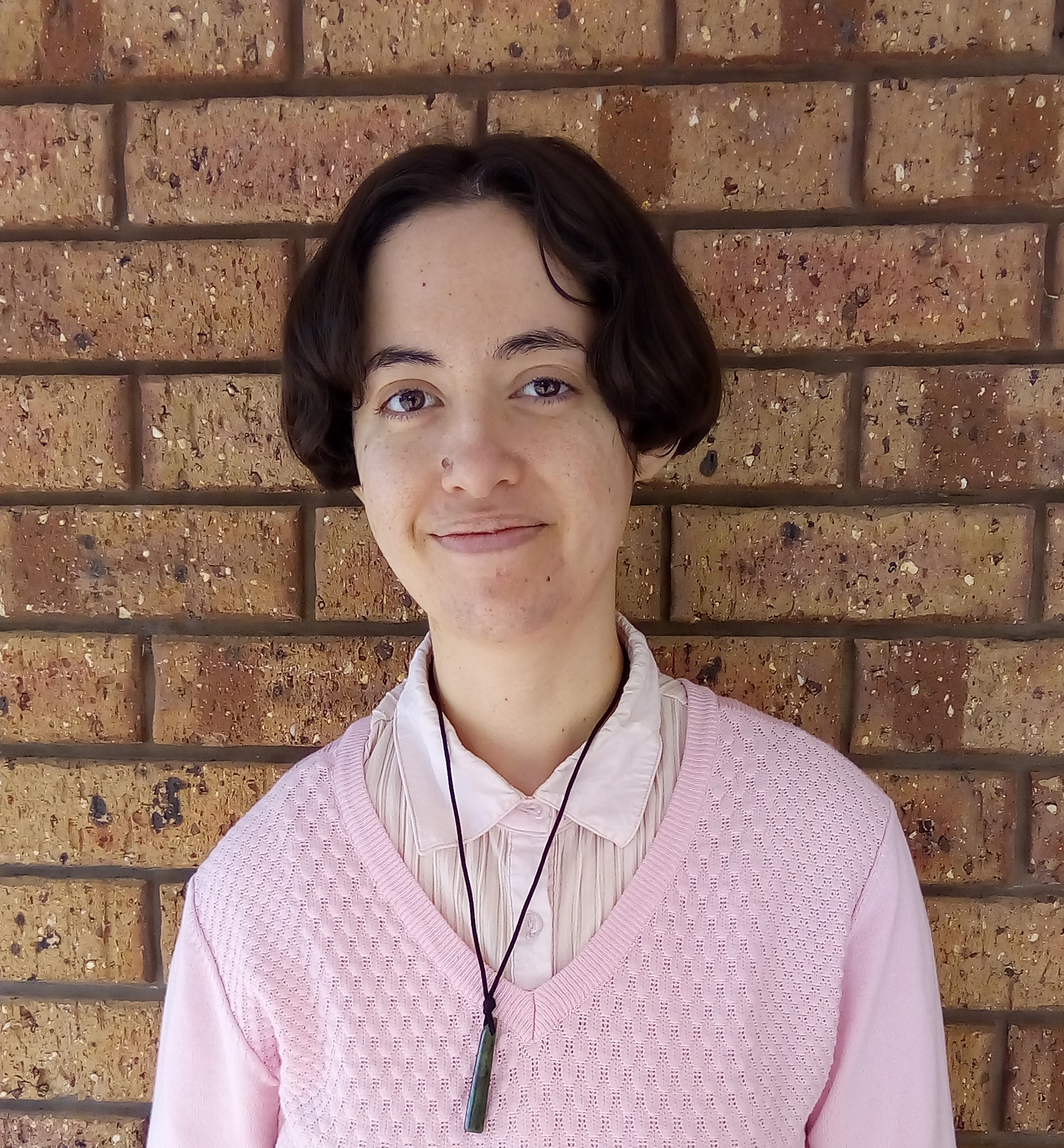 Rosie is smiling at the camera in front of a brown brick wall