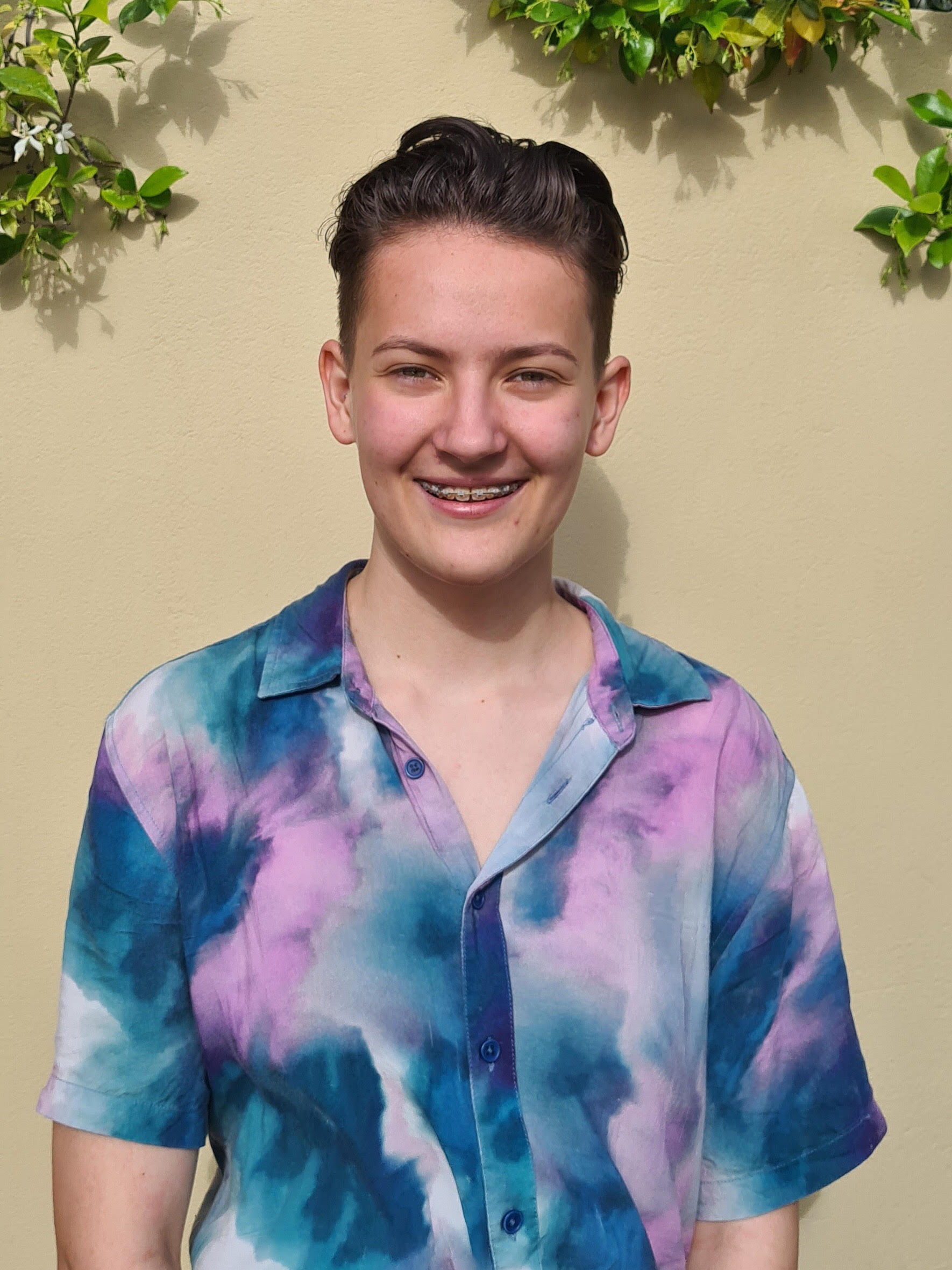 Caitlin stands in front of a wall with greenery, smiling at the camera